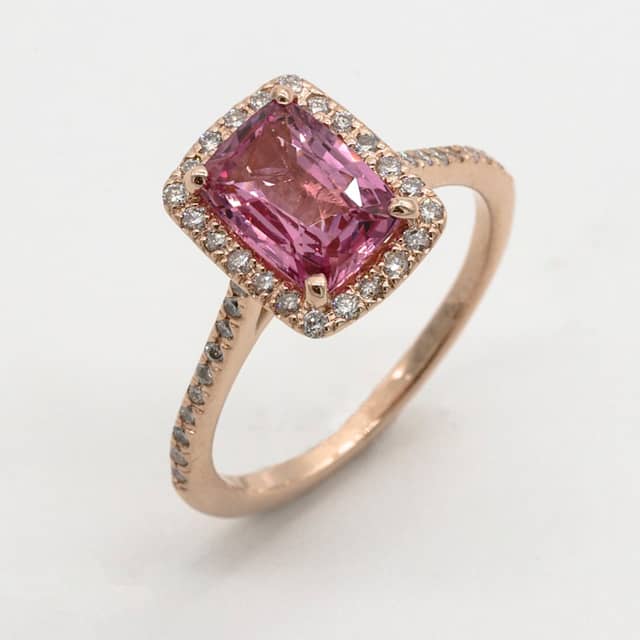 Rose gold ring with a pink cushion-cut gemstone in a halo of small diamonds and a pavé band