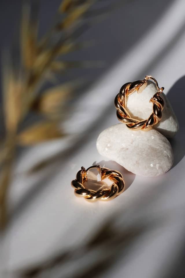 Twisted gold hoop earrings resting on smooth white stones