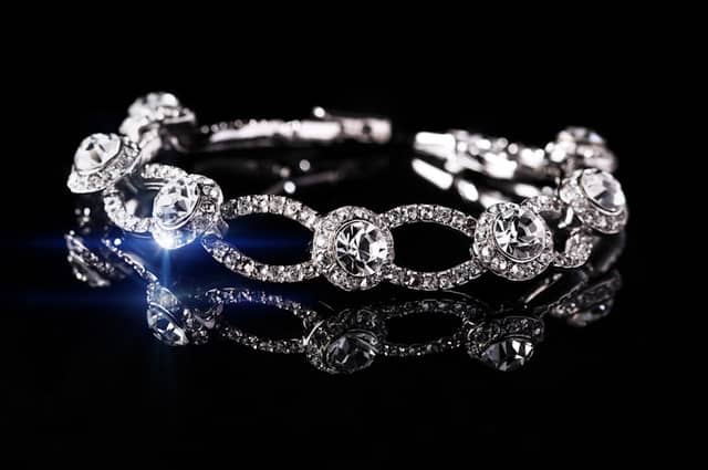 Bracelet of round stones in pavé-set open links on a black surface, with a blue light reflection